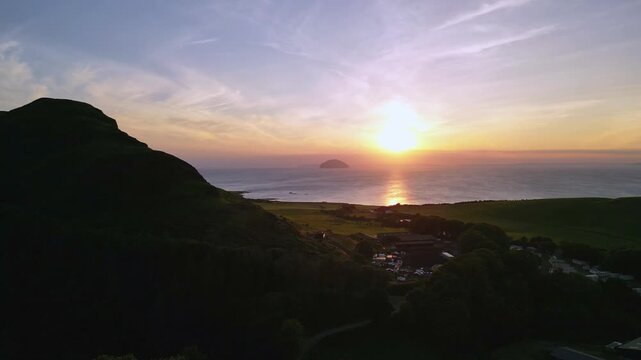 Ailsa Craig Sunset: Aerial drone view of this iconic island, from where all curling stones are hewn, from behind a hill. View out to Irish Sea.