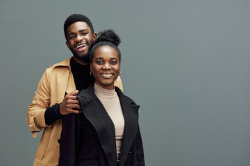 Happy young African couple posing together in stylish outfits against a grey background, showcasing love and connection through bright smiles and modern fashion