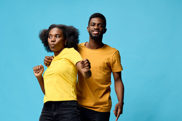 Young African couple joyfully dancing together in vibrant yellow outfits against a bright blue background, expressing happiness and celebration