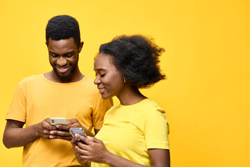 Happy young African couple enjoying their smartphones together against a vibrant yellow background, showcasing modern lifestyle and connection