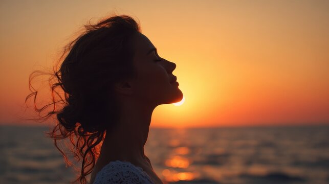 A woman stands at the shore her silhouette framed by a stunning sunset over the ocean. The warm colors of the sky create a peaceful atmosphere during twilight.