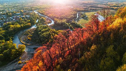 Bright autumn ridge lined with fiery red oaks overlooks a winding river and rural valley, with...