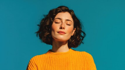 A woman stands confidently with her eyes closed enjoying a moment of calm. Her curly hair frames her face and she wears a cozy yellow sweater that complements the bright blue backdrop.