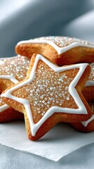 A close-up shot of star-shaped cookies decorated with white icing and sparkling sugar sprinkles, presented on a white surface with a soft, blurred background.