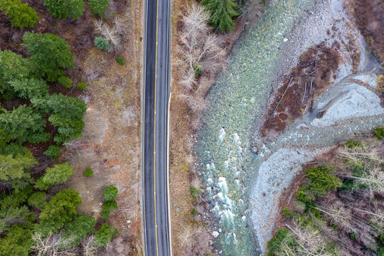 Aerial View Of Narrow Road Through Forest Beside Rocky River In BC, Canada In Winter