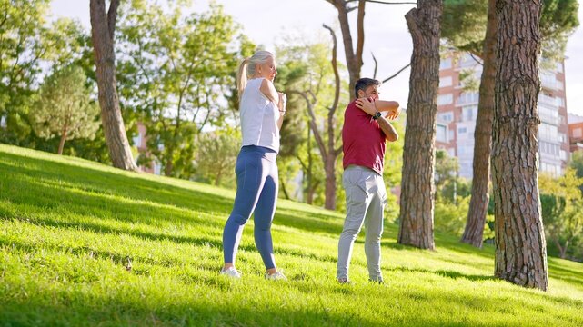 Senior couple stretching arms exercising outdoors in a park