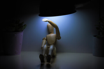 Wooden mannequin sitting under a harsh light, symbolizing stress, harassment, and mental health challenges