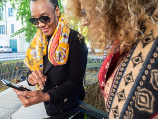 Diverse mature women sharing smartphone outdoors