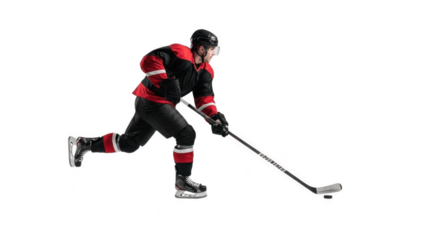 Determined ice hockey player in black and red uniform skating aggressively with stick controlling puck on white background, showcasing speed, balance, power and high‑intensity rink competition

