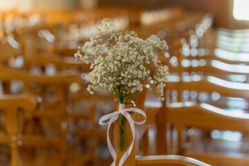 Delicate white flowers adorned on wooden chairs for a wedding ceremony in a charming indoor venue