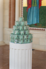 Green decorative glass pieces arranged in a pyramid shape near a religious mural in a serene indoor setting