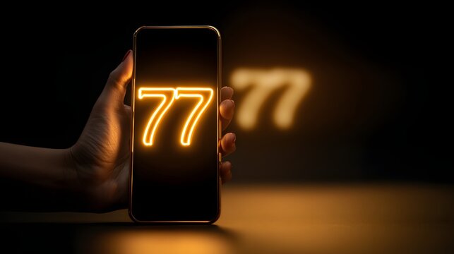 Hand holding smartphone displaying glowing number 77 in dark setting.