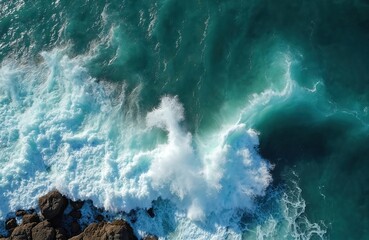 Aerial photo of ocean water waves splashing rocks. Turquoise sea surface forms white foam swirls. Wave breaks at coastline edge creating powerful natural abstract. Vivid colors demonstrate nature