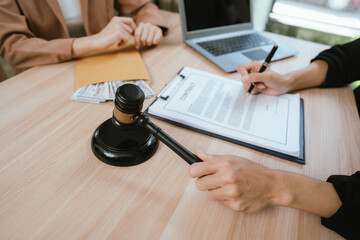 Two professional women discussing legal documents at an office desk, reviewing contracts with a laptop and gavel nearby.