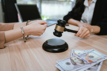Two professional women discussing legal documents at an office desk, reviewing contracts with a laptop and gavel nearby.