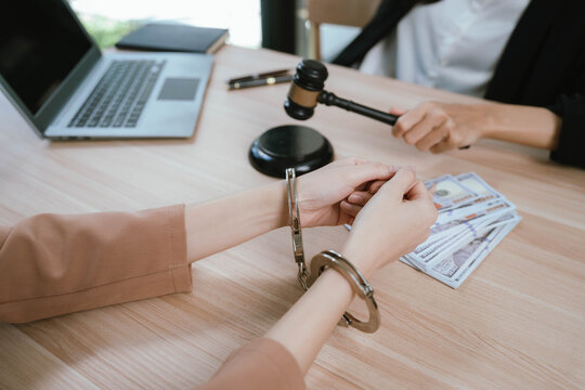 Two professional women discussing legal documents at an office desk, reviewing contracts with a laptop and gavel nearby.