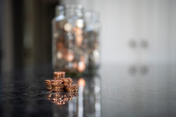 A stack of pennies with change jars in shallow focus behind. Horizontal orientation and copy space.