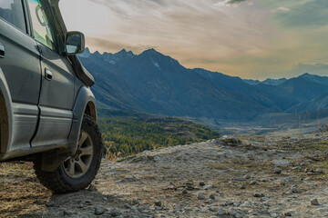 An off-road vehicle with all-terrain tires parked at a mountain road's end, overlooking a vast...