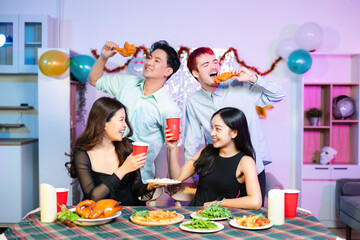 A fun party moment as young friends toast with red cups and laugh while one playfully holds up fried chicken, enjoying food, drinks, and good vibes in a colorful kitchen setting.