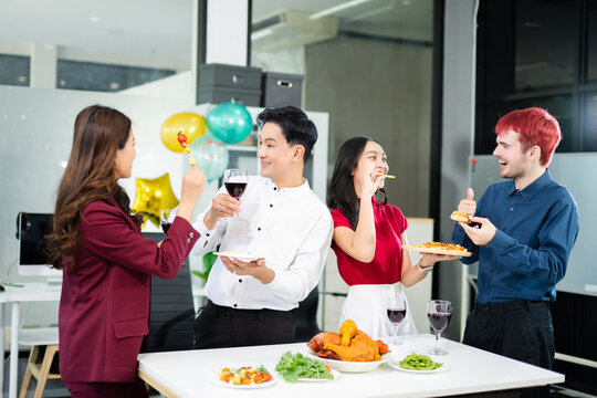Coworkers gather around a modern office table, laughing and enjoying pizza, skewers, and wine, celebrating success in a fun and relaxed workplace setting.