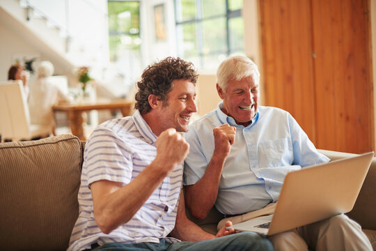 Old man, son and celebration with laptop in home with streaming, goal or sports subscription on sofa. People, elderly father and fist pump with computer, family and excited for game results at house - Powered by Adobe
