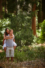 Fototapeta premium Funny, piggyback and couple in forest for vacation, love and bonding together outdoor with partner. Laugh, man and carry woman in woods for holiday adventure, support and explore nature on date