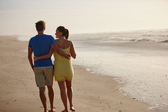 Walking, back and couple by beach for holiday, getaway and vacation in summer together with romance. Embracing, love and man with woman by ocean for bonding, connection or travel with weekend trip.
