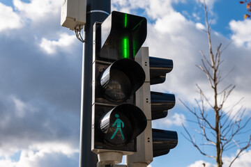 Pedestrian traffic light showing green signal with countdown near its end, only one second remaining for crossing, against a cloudy blue sky.