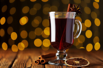Mulled wine with cinnamon and anise star in glass mug against background of glowing garland lights. Winter alcoholic cocktail