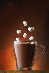 Marshmallows falling into cup of hot chocolate on brown background