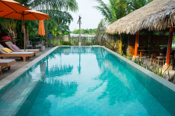 Swimming pool surrounded by stylish lounge chairs with plush cushions and large,  umbrellas. The setting showcases modern,  architecture with warm wood at the villa resort hotel for relax on holiday.