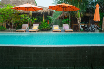 Swimming pool surrounded by stylish lounge chairs with plush cushions and large, umbrellas. The setting showcases modern, architecture with warm wood at the villa resort hotel for relax on  holiday.