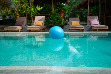 Swimming pool surrounded by stylish lounge chairs with plush cushions and large, umbrellas. The setting showcases modern, architecture with warm wood at the villa resort hotel for relax on  holiday.