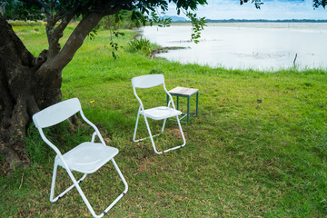 Chairs and table on the grass lawn near the lake with cloud and blue sky background . Our door living to meeting.