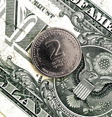 A close-up of an Israeli 2-shekel coin against a backdrop of dollars. The Israeli economy
