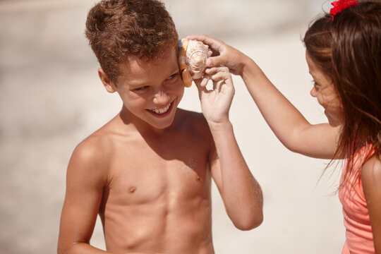 Curious, kids and listening to shell on beach for creative imagination, travel adventure or bonding. Family, children and happy with seashell for ocean sound, sensory stimulation and summer vacation