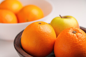 Two different bowls with fresh fruits on a white table. Oranges and apple. Ingredients of nutritious breakfast