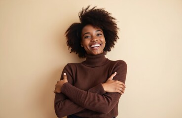 Smiling african woman hugs herself feeling happy and positive. She wears a brown turtleneck and poses against a neutral background. Confident self love and care.