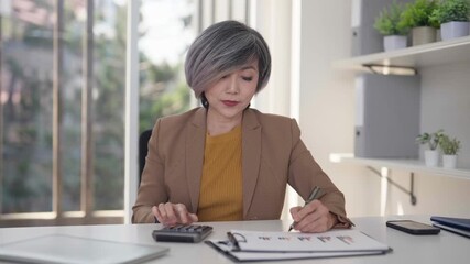 Mature Asian businesswoman analyzes financial data reports professional office setting strategic business planning management executive solutions success focus career growth - Powered by Adobe