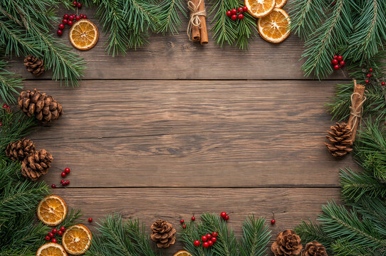 A rustic wooden background framed by pine branches with copy space, pinecones, dried orange slices, and red berries, creating a traditional Christmas or holiday border.