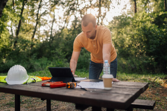 Engineer working with tablet and blueprints in a park