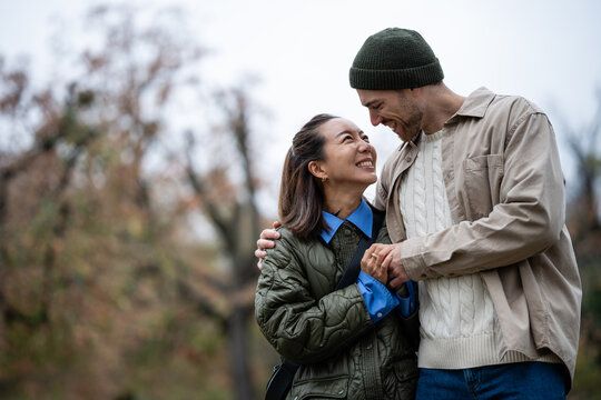 Diverse couple smiling, holding hands enjoying autumn walk
