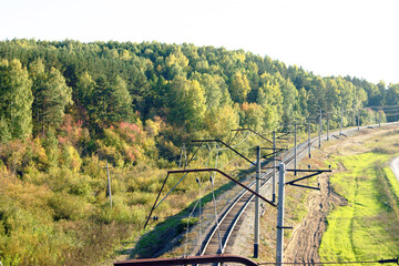 Electrified railway track curving through a rural landscape with a forest in autumn foliage. Represents sustainable transportation infrastructure, regional rail connectivity, green mobility solutions.