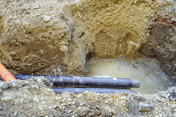 Excavated ground with utility pipes in a deep trench during repair work. Representing urban maintenance, infrastructure renewal, underground utilities, construction workflow, and municipal services.