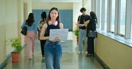 Indian young gen z busy woman lady hold laptop in hand look screen check new email notes walk campus place. Teen girl female use device do exam study online e learning work skill data day time