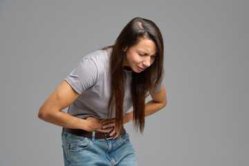 Woman bending forward and holding abdomen in pain, studio scene on neutral grey
