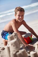 Portrait, smile and kid with sandcastle at beach for travel, sand sculpting and holiday adventure. Happy, child and boy with bucket for playful fun, seaside activity and creative games on vacation
