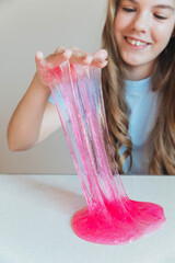 Girl lifting and stretching a thick, glossy stream of vibrant pink slime. Fun sensory toy and trendy DIY activity