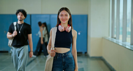 Indian young adult gen z female lady confident student standing hold bag pack fold hand look camera indoor campus place happy smiling girl cross arms staring cam do casual pose enjoy new college