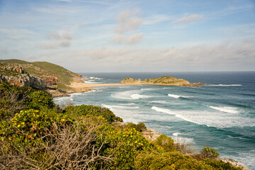 Natural ocean coastline featuring clear blue water, gentle waves, and green coastal cliffs. A serene landscape perfect for travel, nature, and outdoor photography.